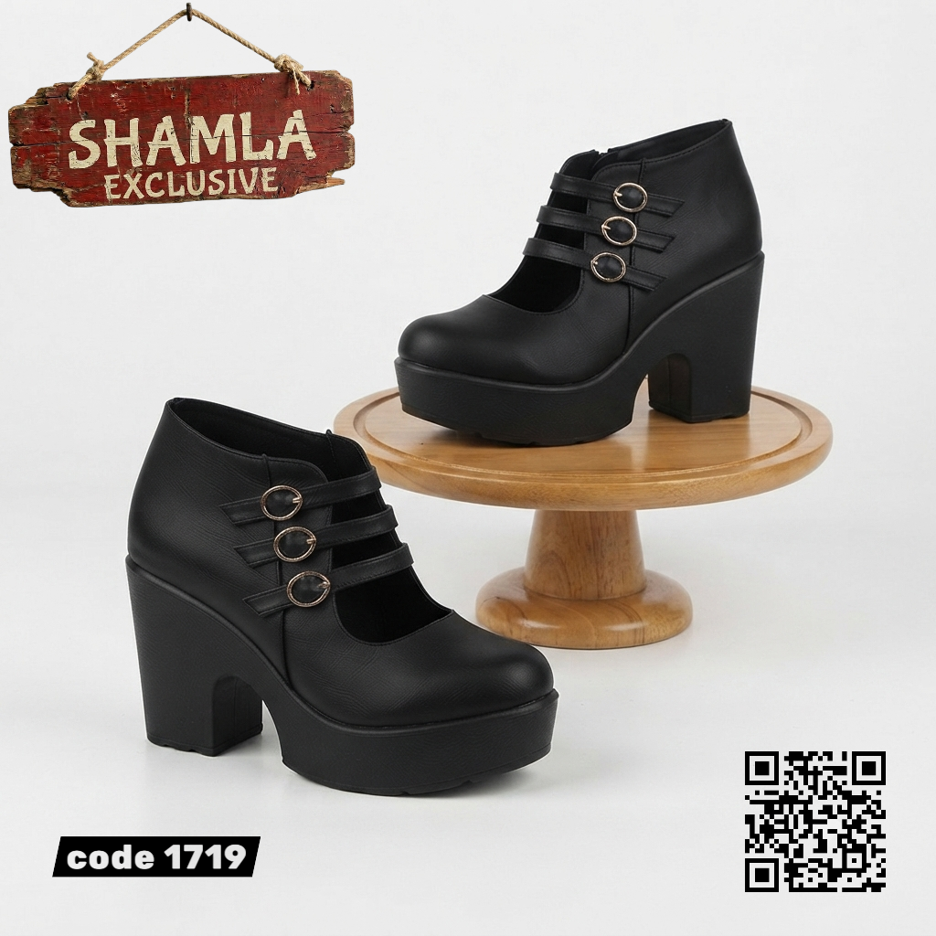 A pair of black platform ankle boots with a block heel and three decorative metal rings on the side, shown on a white background with a wooden display stand, a hanging 'SHAMLA EXCLUSIVE' sign, a product code label, and a QR code.

